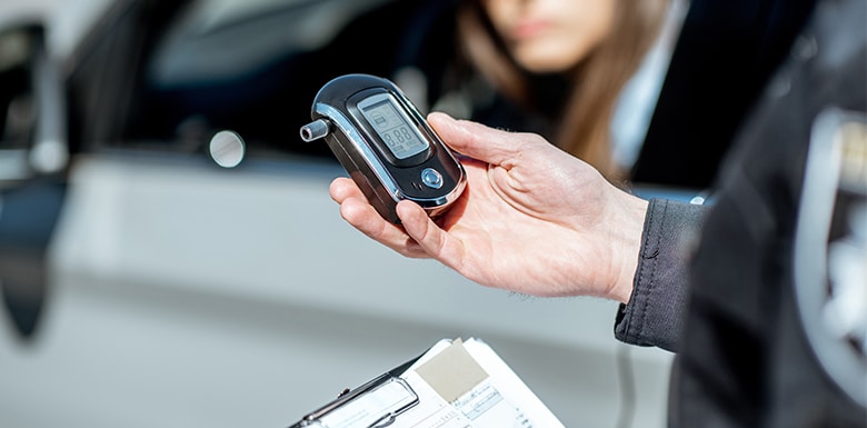 Police officer in Pennsylvania at a traffic stop conducting a breath DUI Test. Light grey sedan with female driver blurred in the background.